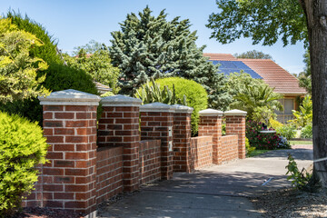 Brick fence with decorative pillars lining a suburban residential sidewalk in Australia. Concept of home frontage design, neighborhood lifestyle, boundary, and residential property environment.