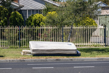 Discarded mattress placed on a grassy roadside verge in a suburban residential street in Melbourne, Australia. Concept of urban waste, illegal dumping, local council maintenance,household rubbish