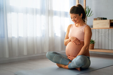 Relaxed pregnant woman doing breathing exercises while sitting on an exercise mat at home