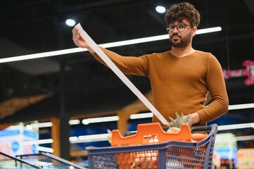 Shopper checking long receipt while shopping groceries in supermarket
