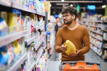 Arab man choosing detergent in supermarket while shopping for groceries
