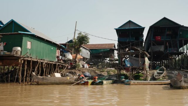 Wooden boats float near tall stilt houses in a Cambodian riverside village
