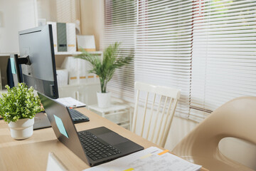 Fototapeta premium Home office workspace for business features modern computer desk with laptop, monitor, organized documents, green plants, and inviting chair, promoting productive work environment
