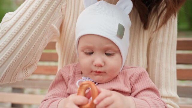 Mother Calms Infant, Caucasian Mother Gently Reassures Baby Chewing Toy On Park Bench, Mother Of Caucasian Appearance Lovingly Comforts Her Curious Baby Playing With Teether On Bench Amid Trees