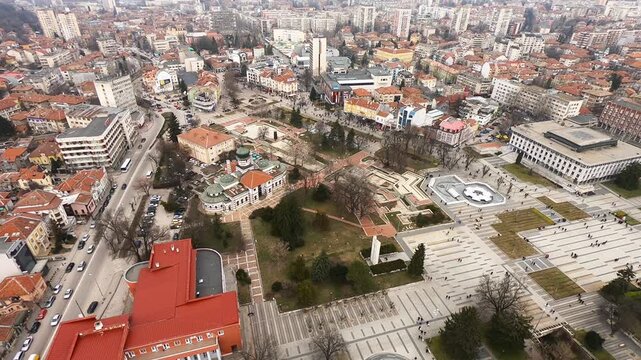 Drone video of Pleven center on March 3, 2019, showing landmarks, the square, the Ossuary, church, municipal building, fountains, and people walking with a long national flag, Pleven, BG,03 March 2019