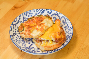 A bagel with pickled jalapeno, cheese, and egg on a wooden table. Breakfast concept.