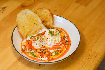 Turkish egg with sourdough bread in a white dish on a wooden table.
