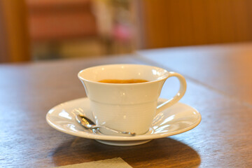 Hot americano in a white cup on a wooden table in a warm light at a coffee shop.
