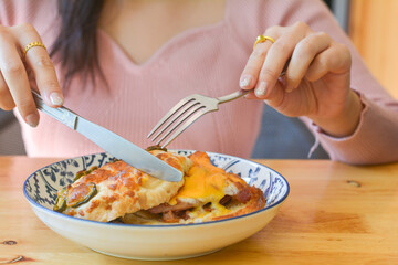 A woman is eating a bagel with pickled jalapeno, cheese, and egg on a wooden table. Breakfast concept.