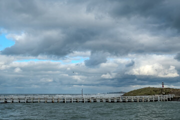 Obraz premium Nieuwpoort, West-Vlaanderen, Belgium, Ocotber 25th, 2025, Serene harbor with guiding lighthouse, Quiet seaside pier leading to small lighthouse amid moving sky and tranquil