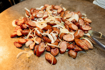Grilled sausage slices cooked with sauteed onions on a hot griddle. Juicy, browned meat and caramelized onions create a rustic, hearty food presentation with warm, appetizing tones