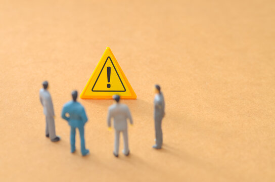 Miniature Business Team Analyzing a Yellow Warning Sign and Discussing Risk Management - Powered by Adobe
