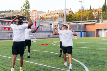 Group of diverse football players cheering and celebrating a goal on a green soccer field during a training session