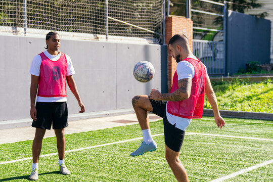Young men wearing bibs practicing ball control on a sunny football pitch, training for a sports game - Powered by Adobe