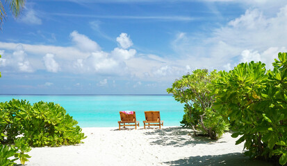 Beautiful tropical beach with white sand and two sun loungers on background of turquoise ocean and...