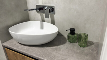 Modern bathroom sink with white ceramic basin, wall mounted chrome faucet and green glass accessories on gray stone countertop in minimalist interior design