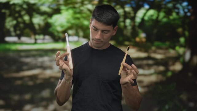 Young hispanic man holds electric toothbrush and bamboo toothbrush side by side in green park; sustainable choice.