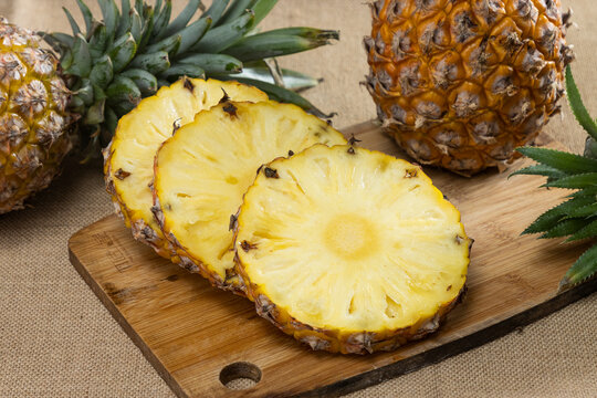 Fresh yellow pineapple fruit sliced on wooden cutting board with a knife