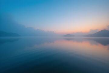 Fototapeta premium Misty sunrise over a calm lake with mountain reflections