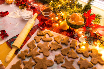 Unbaked Christmas cookies in festive shapes arranged on parchment paper. Holiday baking process with gingerbread dough, cookie cutters and warm seasonal kitchen atmosphere.