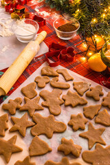 Unbaked Christmas cookies in festive shapes arranged on parchment paper. Holiday baking process with gingerbread dough, cookie cutters and warm seasonal kitchen atmosphere.