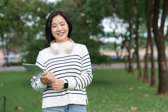 Young asian woman holding tablet in park - Powered by Adobe