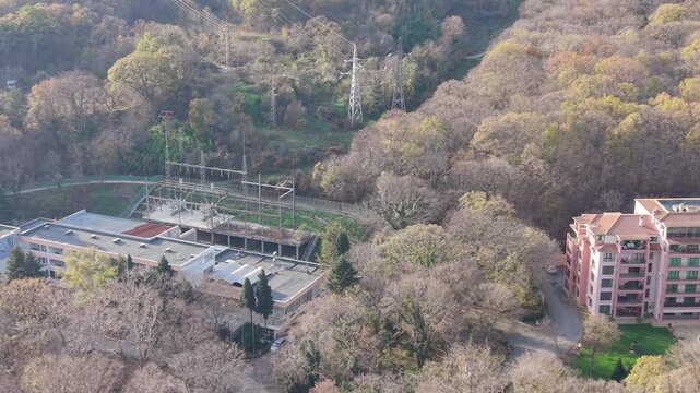Aerial drone footage showing residential buildings surrounded by wooded hills and valleys, highlighting urban development integrated with natural landscape under soft daylight.