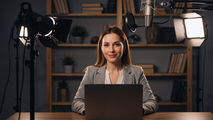 Woman sitting at desk recording video with laptop, microphone, light for studio streaming from home. Online broadcasting and content creation.