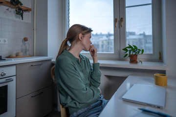 Stressed worried woman sits at table nervously biting nails overwhelmed by thoughts. Tired anxious female pensive looking to window lack motivation, feeling emotional exhaustion, uncertainty at home.