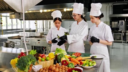 Chef instructor teaching two young culinary students in a commercial kitchen during a professional cooking class with fresh vegetables. Ideal for chef training, gastronomy, and food education themes.