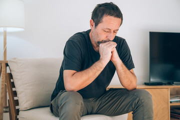 Authentic middle-aged caucasian man with beard, hands clasped, looking worried and deep in thought. Mental health, stress, crisis, and midlife themes.