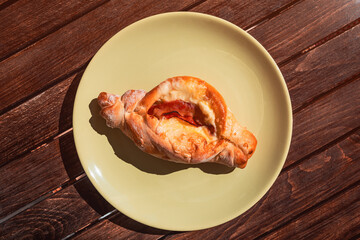 Traditional Greek peinirli with melted cheese and cured meat on a beige plate, served on a wooden table under natural sunlight. Savory Mediterranean pastry.