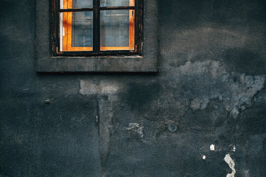 Close-up of a worn wooden window with peeling paint set in a dark, weathered and cracked plaster wall. Moody texture for decay, abandonment, poverty, history, urban exploration concepts.