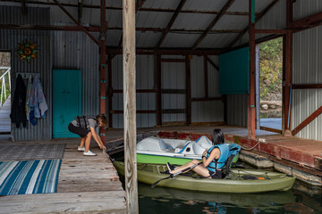 Two kids docking kayaks inside a rustic boathouse on calm lake water