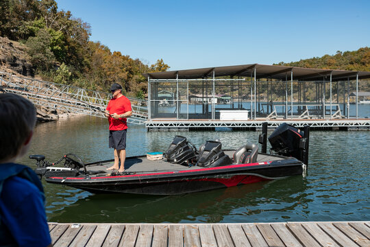 boy standing on deck and  watching dad fish off of bass boat