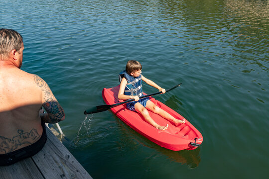 father sitting on dock watching son kayak