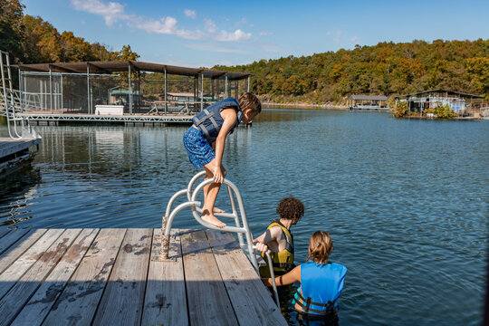 Kid and teenagers in lifejackets preparing to swim from  lakeside dock