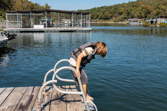 boy standing on swim ladder looking down at lake
