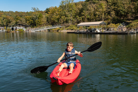Boy paddling a red kayak on a calm lakeside with docks and trees