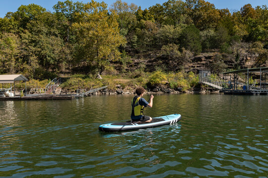 Person on knees paddling on a paddle board on lake near shore