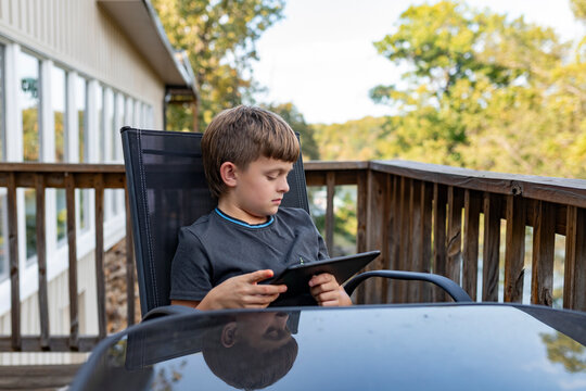 Child sitting on a deck chair using a tablet beside  wooden railing