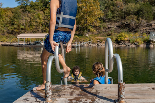child sitting on ladder watching people swim in lake