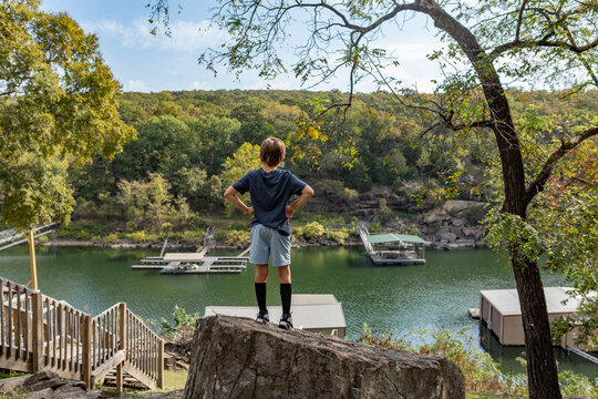 boy with hands on hips standing on rock looking at a  lake