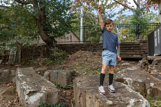 boy standing on boulder holding rock in air