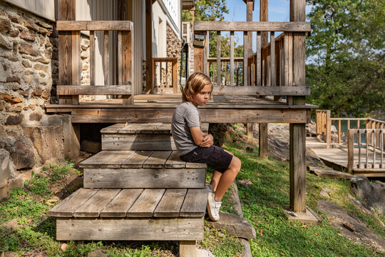 Child sitting on wooden steps beside a cabin on a grassy hillside