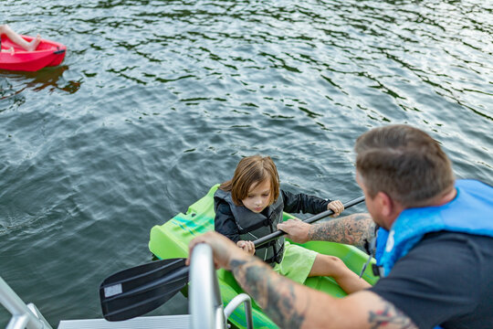 father handing child paddle for kayak on lake