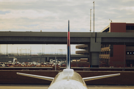 The tail of a commercial jet stands beneath an overpass.