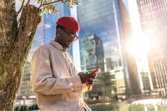 Young man using smartphone leaning on tree in city - Powered by Adobe