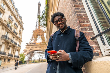 African man smiling, visiting paris and using smartphone near eiffel tower