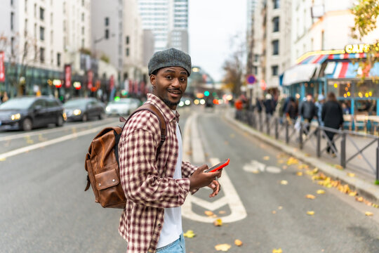 Young man crossing urban street smiling using smartphone